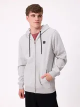 Campera canguro de felpa color gris claro melange, con capucha ajustable mediante cordones negros, cierre frontal completo, bolsillos tipo canguro y parche con logo de la marca en el pecho.