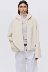 Campera de tejido suave con efecto de piel sintética, corte holgado y hombros caídos. Presenta capucha forrada, cierre frontal con cremallera y bolsillos laterales ocultos en las costuras.