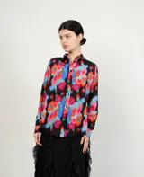 Camisa de manga larga con estampado floral multicolor sobre fondo negro, cuello clásico y cierre frontal de botones.