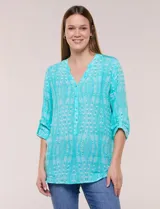 Blusa turquesa de silueta suelta confeccionada en tejido liviano, con escote en V, pequeña cartera frontal con botones decorativos y mangas 3/4 con presilla para arremangar. Presenta patrón estampado geométrico tipo tie-dye y ruedo curvo.