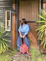 Bolso tipo tote bag de tamaño mediano confeccionado en tela con estampado paisley rojo y blanco, con asas de cuero marrón.
