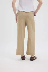 Pantalón de lino color beige, de silueta relajada, tiro medio-alto, cintura elastizada con cordón ajustable, bolsillos laterales y bolsillos traseros.