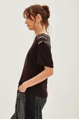 Remera de viscosa color negro, con cuello redondo y mangas cortas. Presenta un detalle decorativo de apliques metálicos en forma de corazón dispuestos en líneas sobre los hombros.
