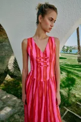 Vestido largo sin mangas con escote en pico y tirantes anchos. Presenta un diseño de rayas verticales en tonos fucsia y rojo, con detalle de falsos botones frontales y cierre de cremallera oculto en la espalda.