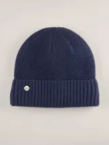 Gorro tipo beanie color azul marino, con textura tejida en la parte superior y borde acanalado. Incluye un pequeño aplique metálico circular con el logo de la marca en el frente.