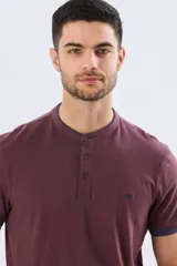 Remera estilo polo con cuello mao y manga corta, de color bordó con detalles en azul en los bordes de las mangas y cuello. Cuenta con cierre frontal parcial de tres botones y pequeño logo bordado en el pecho.