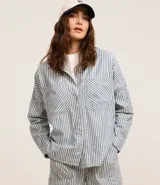 Camisa de jean de manga larga con diseño de rayas verticales, cuello inglés, cierre frontal con botones y dos bolsillos grandes en el frente.