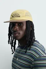 Gorra de 5 paneles de color amarillo claro con tejido ripstop, visera plana marrón de efecto desgastado y bordado frontal en negro. Cuenta con ajuste en la parte posterior.