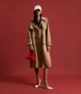 Trench coat largo de corte evasé confeccionado en gabardina de poliéster. Presenta cuello con solapas, aleta en los hombros, cierre frontal con botones y cinta para lazo en la cintura.