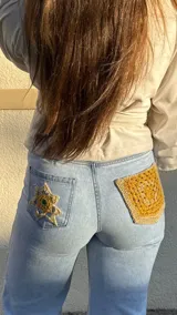 Pantalón de jean celeste de corte recto con roturas en las rodillas y detalles de crochet artesanal y pedrería en la parte trasera.