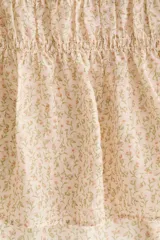 Blusa de lyocell con estampado floreado pequeño sobre base beige, escote redondo con tiras decorativas para atar, busto fruncido, mangas cortas abullonadas con elástico y ribete de volado, y bajo levemente acampanado.