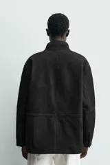 Parka de cuero color negro, de corte relajado, con cuello alto, cierre frontal con cremallera oculta y solapa con botones a presión. Cuenta con bolsillos frontales tipo cargo con solapa en la cadera y bolsillos de vivo en el pecho.