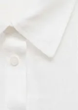Camisa de lino blanca con cuello camisero, cierre frontal de botones y bolsillo de parche en el pecho. Presenta mangas largas con puños abotonados y un diseño recto.