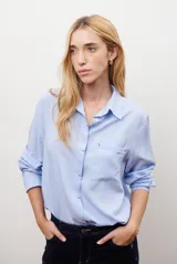 Camisa blanca de manga larga con cuello clásico, cierre de botones frontal y bolsillo de parche en el pecho.