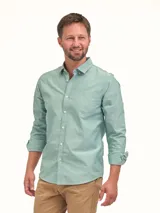 Camisa de manga larga en color verde claro, confeccionada en tejido de algodón con textura sutil. Presenta cuello clásico con botones, cierre frontal abotonado y un bolsillo en el pecho con detalle bordado.