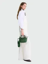 Bolso pequeño tipo crossbody de cuero verde, con doble asa corta, solapa con cierre de broche a presión, correa ajustable y extraíble, y costuras decorativas en contraste.