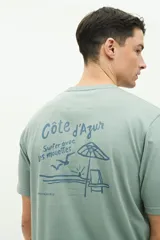 Remera de manga corta color verde agua con estampado gráfico en la espalda que incluye texto y motivos playeros. Confeccionada en algodón con calce regular.