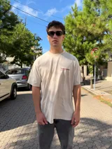 Remera de corte oversize color beige, con estampado gráfico en la espalda en color bordó que incluye el logo y texto descriptivo.