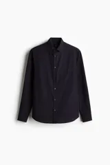 Camisa negra de manga larga con cuello inglés, tapeta clásica, bolsillo superior abierto y canesú con pliegue de caja en la espalda. Los puños tienen cierre ajustable de botón y el bajo es redondeado.