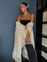 Ruana tejida a mano en punto arroz con lana merino, presenta un diseño envolvente con flecos en los extremos.