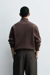Jersey de punto de corte regular, color gris oscuro, con cuello subido y cierre frontal de cremallera. Presenta mangas largas y acabados en rib en puños y ruedo.