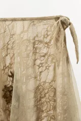 Falda corta de tiro bajo confeccionada en tul color beige, con capas, bajo asimétrico, bordados florales oscuros con lentejuelas en contraste y cierre lateral con nudo.