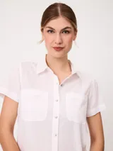 Camisa de manga corta color beige, confeccionada en mezcla de algodón y lino, con cuello camisero, cierre frontal de botones y dos bolsillos aplicados en el pecho.