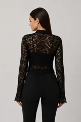 Top de encaje negro con mangas largas acampanadas, cuello mao con cierre de lazo frontal y diseño ajustado al cuerpo.