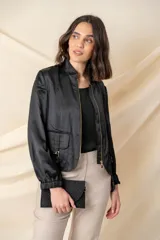 Campera tipo bomber color negro, confeccionada en tejido satinado. Presenta cierre frontal metálico, bolsillos laterales con hebillas decorativas doradas y puños elásticos.