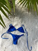 Bikini de lycra azul, compuesto por corpiño de triángulos movibles con breteles regulables y espalda para atar, y bombacha colaless regulable a los costados.