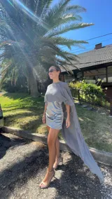 Vestido corto de satén con frunces laterales y acabado brillante, que incluye una capa desmontable de gasa transparente que se puede colocar de diversas formas.