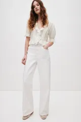 Blusa color blanco crudo, de escote en V pronunciado con ribetes de volado, mangas abullonadas al codo y detalles de alforzas, encaje y bordados en el frente.