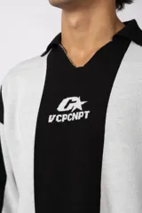 Sweater de tejido de punto con diseño de rayas verticales en tonos beige y blanco. Presenta cuello polo abierto, mangas largas y un corte holgado. Incluye un logo bordado en el centro del pecho.