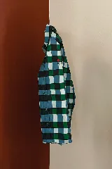 Camisa de manga larga con estampado de cuadros en tonos azul, verde y negro. Presenta cuello clásico, cierre frontal con botones y un pequeño bordado de una flor roja en el pecho.