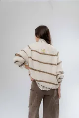 Buzo de tejido de punto grueso en color gris con rayas horizontales en color crema, de corte holgado, cuello redondo y mangas largas.