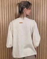 Camisa color beige de lino con mangas abullonadas tres cuartos y cierre frontal mediante múltiples lazos para atar.