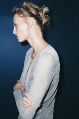 Chaqueta gris de punto fino semitransparente con hilo metalizado, cuello redondo, manga larga y cierre frontal con botones.