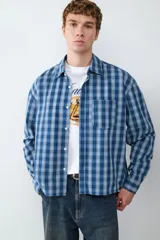 Camisa de mangas largas color azul con estampado a cuadros blancos, de corte boxy. Presenta cierre frontal con botones, cuello con solapa y un bolsillo en el pecho.