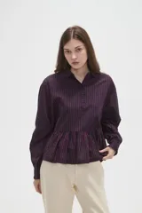 Camisa de manga larga con estampado de rayas verticales en azul marino y rojo. Presenta cuello camisero, cierre frontal con botones y un diseño con volado en la cintura que aporta volumen.