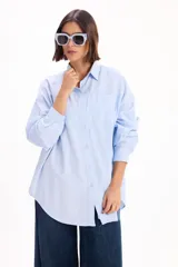 Camisa de corte oversize color celeste, con cuello clásico, cierre frontal de botones y mangas largas con puños abotonados.