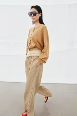 Pantalón de tiro medio con diseño de rayas verticales en tonos beige y marrón. Presenta una cintura elástica ajustable con cordones, bolsillos laterales ocultos y corte de pierna recta con aberturas en el bajo.