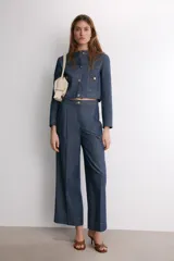 Pantalón de tiro medio confeccionado en denim azul oscuro, con diseño de pierna ancha, pinzas frontales y pespuntes a contraste. Cuenta con cierre frontal de cremallera y botón.