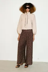 Pantalón de tiro alto con pernera ancha y diseño fluido. Presenta un estampado de lunares blancos sobre fondo marrón y detalle de frunces en la cintura.