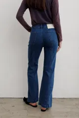 Jean de denim azul de tiro medio, con corte flare y costuras frontales destacadas.