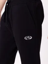 Babucha jogger color gris oscuro, con cintura elástica ajustable con cordón, bolsillos laterales y puños elásticos en los tobillos. Presenta un logo estampado en el muslo izquierdo.