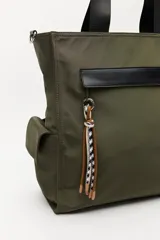 Bolso tipo tote color negro, con doble asa superior y correa desmontable. Presenta un bolsillo frontal con solapa, bolsillos laterales y un detalle colgante decorativo con tiras de colores.