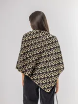 Poncho liviano con diseño geométrico de letras entrelazadas en color negro y beige. Presenta un corte asimétrico y caída fluida, ideal para superponer sobre otras prendas.