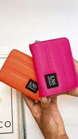 Billetera corta de diseño capitoneado con cierre perimetral y solapa frontal. Cuenta con compartimentos internos para tarjetas y billetes, e incluye una correa de mano desmontable.