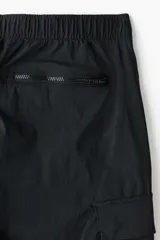 Pantalón cargo negro de nylon, de corte regular con cintura elástica ajustable con cordón. Cuenta con bolsillos laterales con cierre, bolsillos cargo con solapa en las piernas, bolsillos traseros con cierre y tensores en los tobillos.