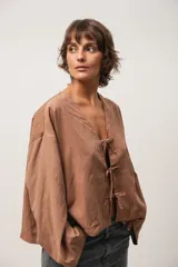 Blusa marrón de corte crop, escote en V y mangas largas anchas. Cierre frontal con lazos.